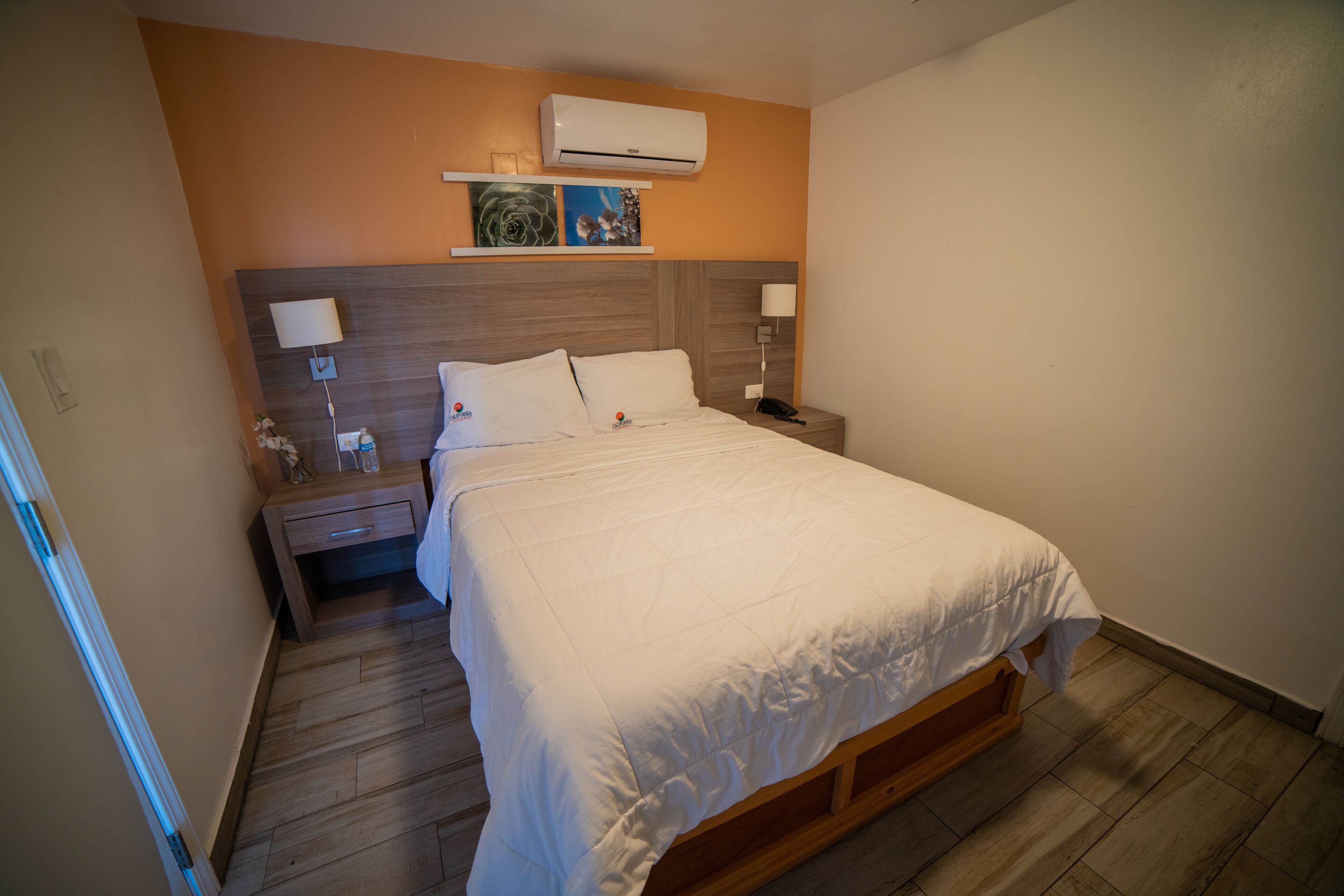 A neatly made bed with white bedding, a wooden headboard, and a nightstand with a lamp and phone.