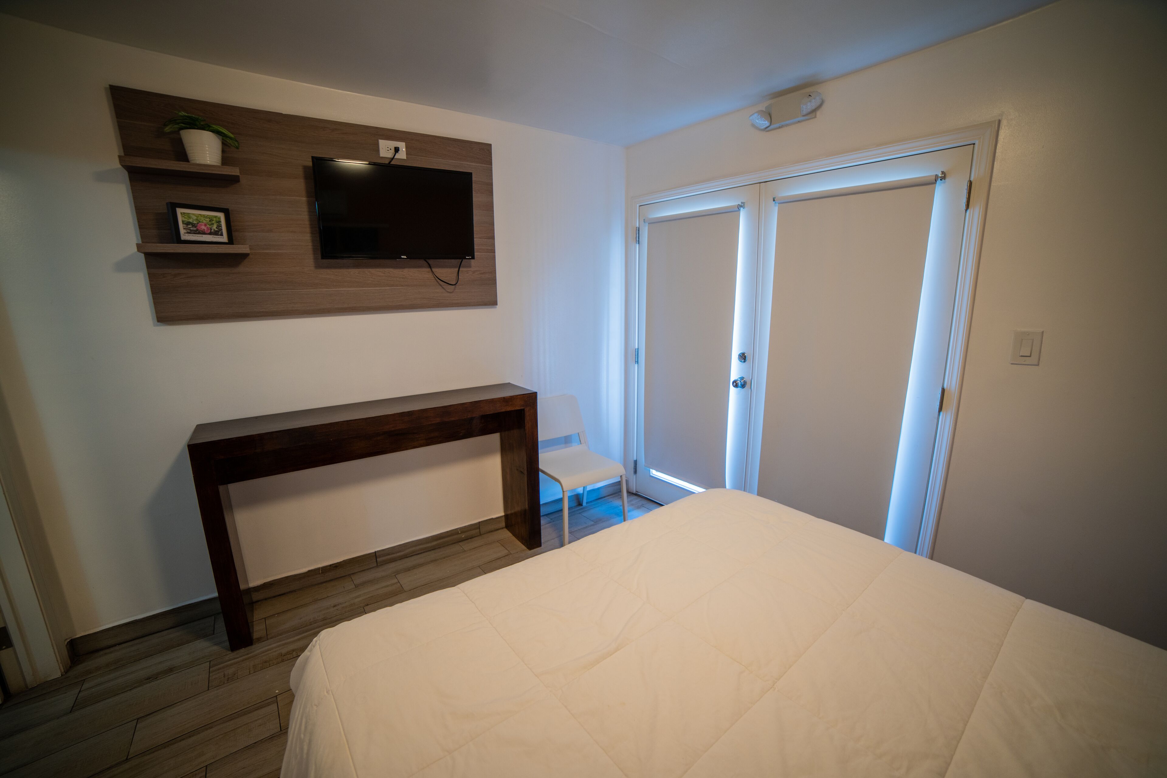 A bedroom with a bed, a TV mounted on the wall, a desk, and a chair.