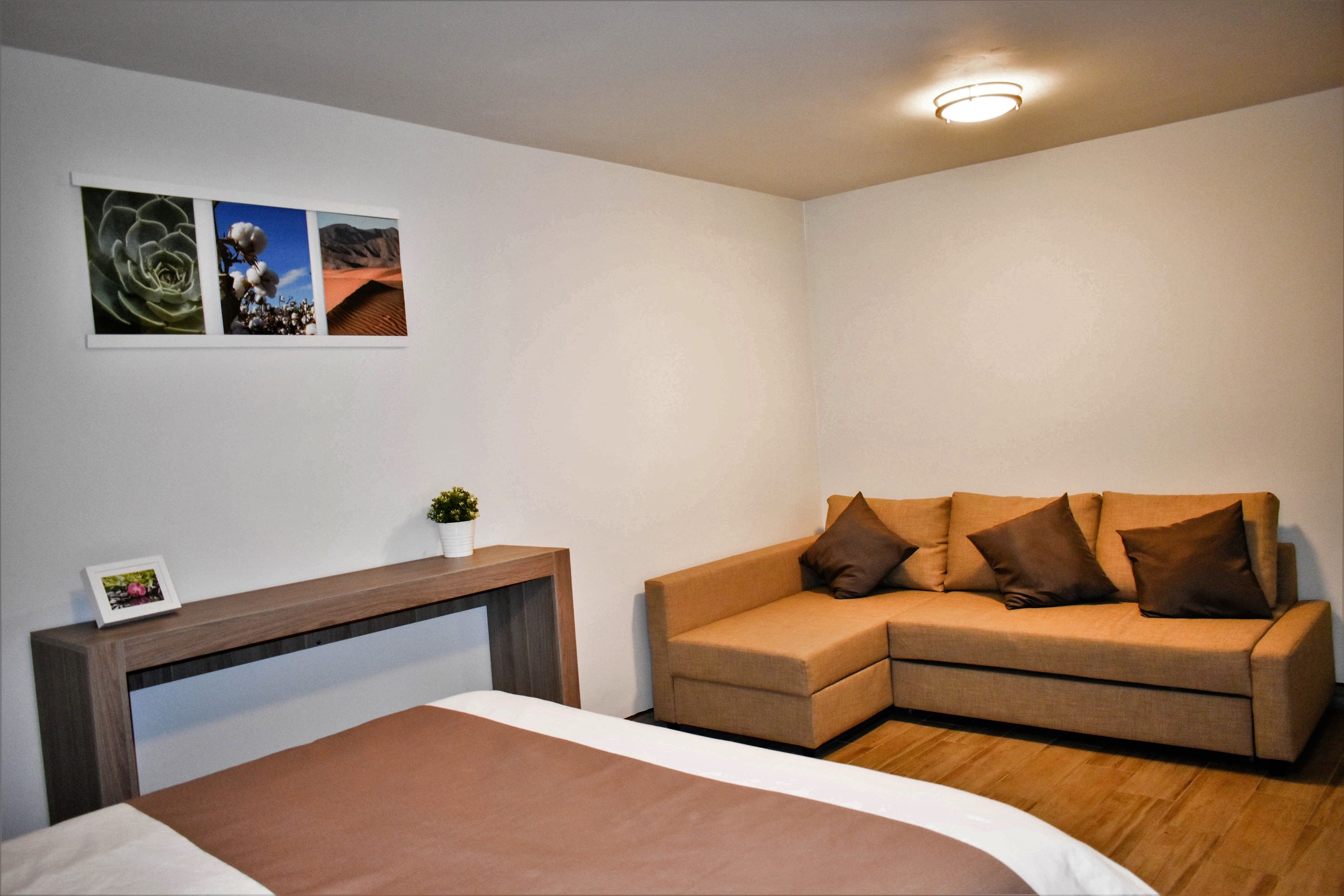 A modern bedroom with a bed, a wooden console table, a brown sofa, and three framed pictures on the wall.