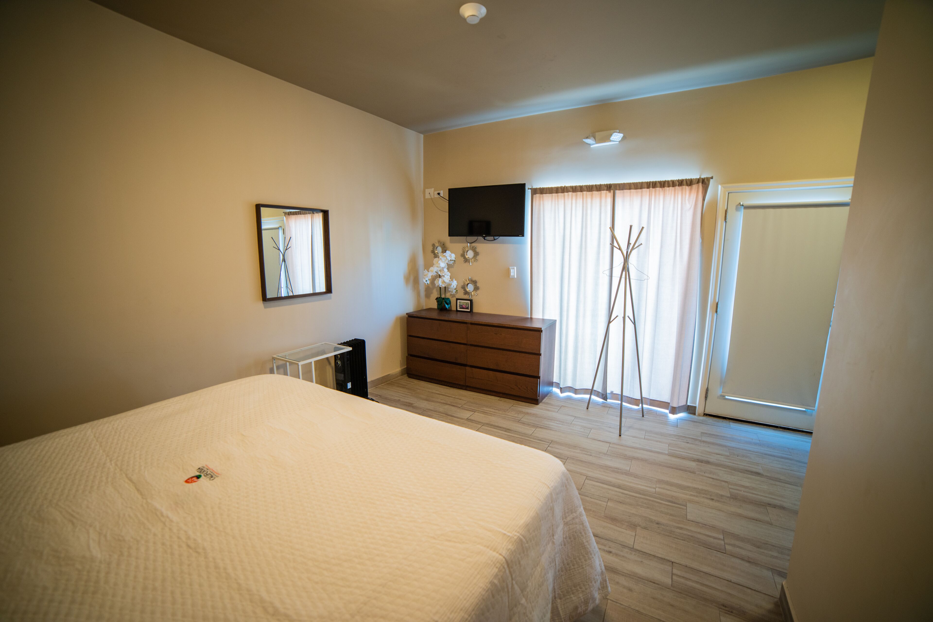 A bedroom with a bed, dresser, TV, and a window with curtains.