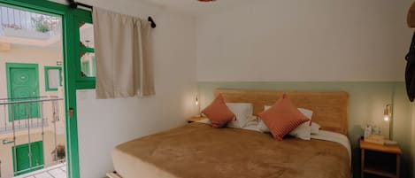 A bedroom with a bed, a nightstand, a hanging lamp, and a view of a green building outside.