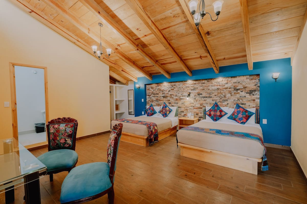 Una habitación con dos camas, suelo de madera, pared de ladrillo decorativa y techo con vigas a la vista.