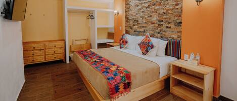 A bedroom with a wooden bed, a brick-patterned headboard, a wooden dresser, and a TV mounted on the wall.