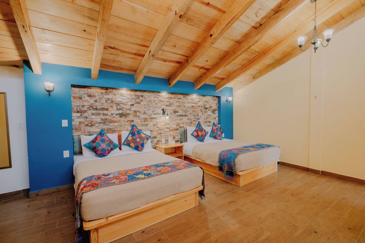 Un dormitorio con dos camas, un cabecero de ladrillo, vigas de madera y una pared azul decorativa.