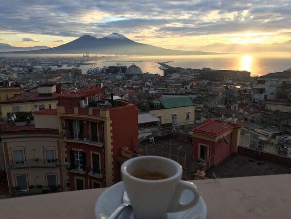 A cup of coffee on a balcony overlooking a cityscape with a mountain in the background. - Santa Caterina B&B (Naples)