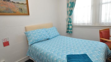 Ein Einzelbett mit einem blauen und weißen Musterzudecke, ein blaues Handtuch, ein roter Stuhl und ein Bild an der Wand.