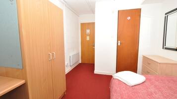 A hotel room with a red carpet, wooden wardrobe, a white bed with a white blanket, a wooden dresser, and a mirror on the wall.