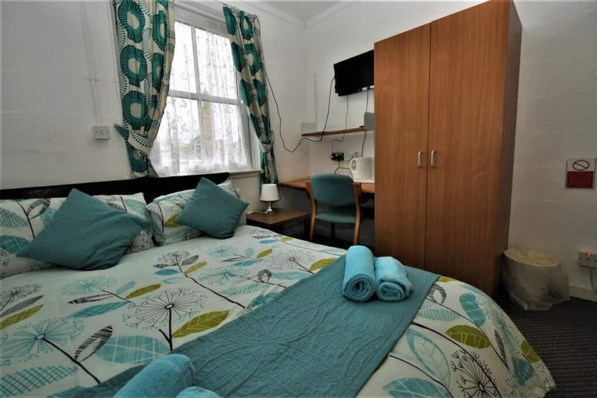 A hotel room with a bed, a desk, a chair, a wardrobe, and a television on the wall.