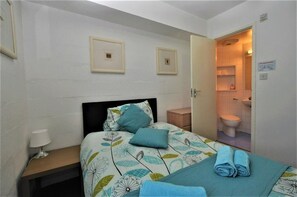 A bedroom with a bed, pillows, a bedside table with a lamp, and a bathroom visible through an open door. - Waterfront Guest Accommodation (Greenock)