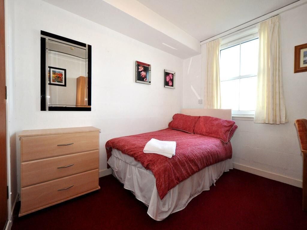 Un dormitorio con cama, cómoda, ventana con cortinas y cuadros en la pared.