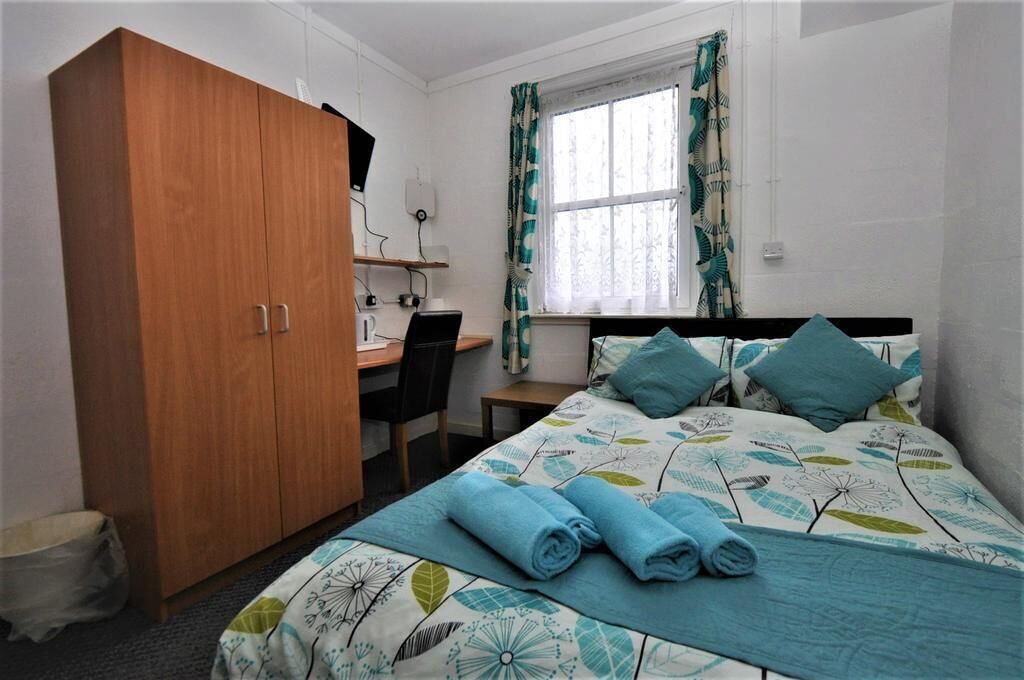 A bedroom with a bed, a desk, a wardrobe, and a window with curtains.