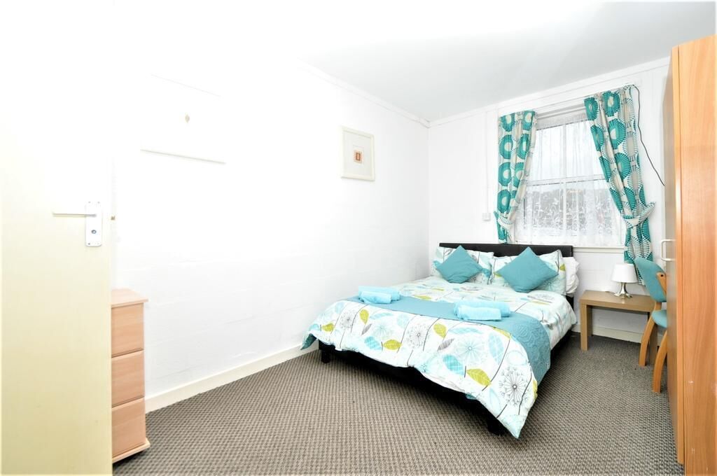 A bedroom with a bed, a dresser, a nightstand, a lamp, and a window with curtains.