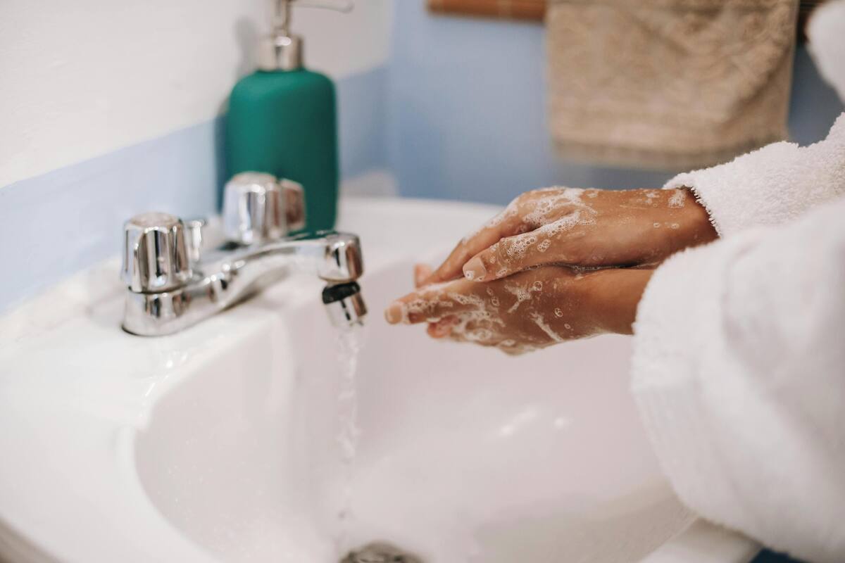 A hand washing at a sink with a faucet and soap dispenser.