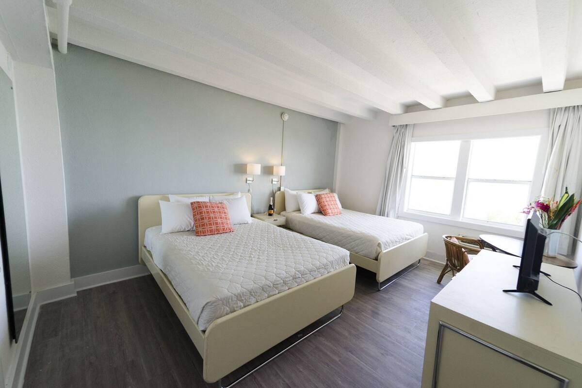 A hotel room with two beds, a desk, a chair, and a window with curtains.