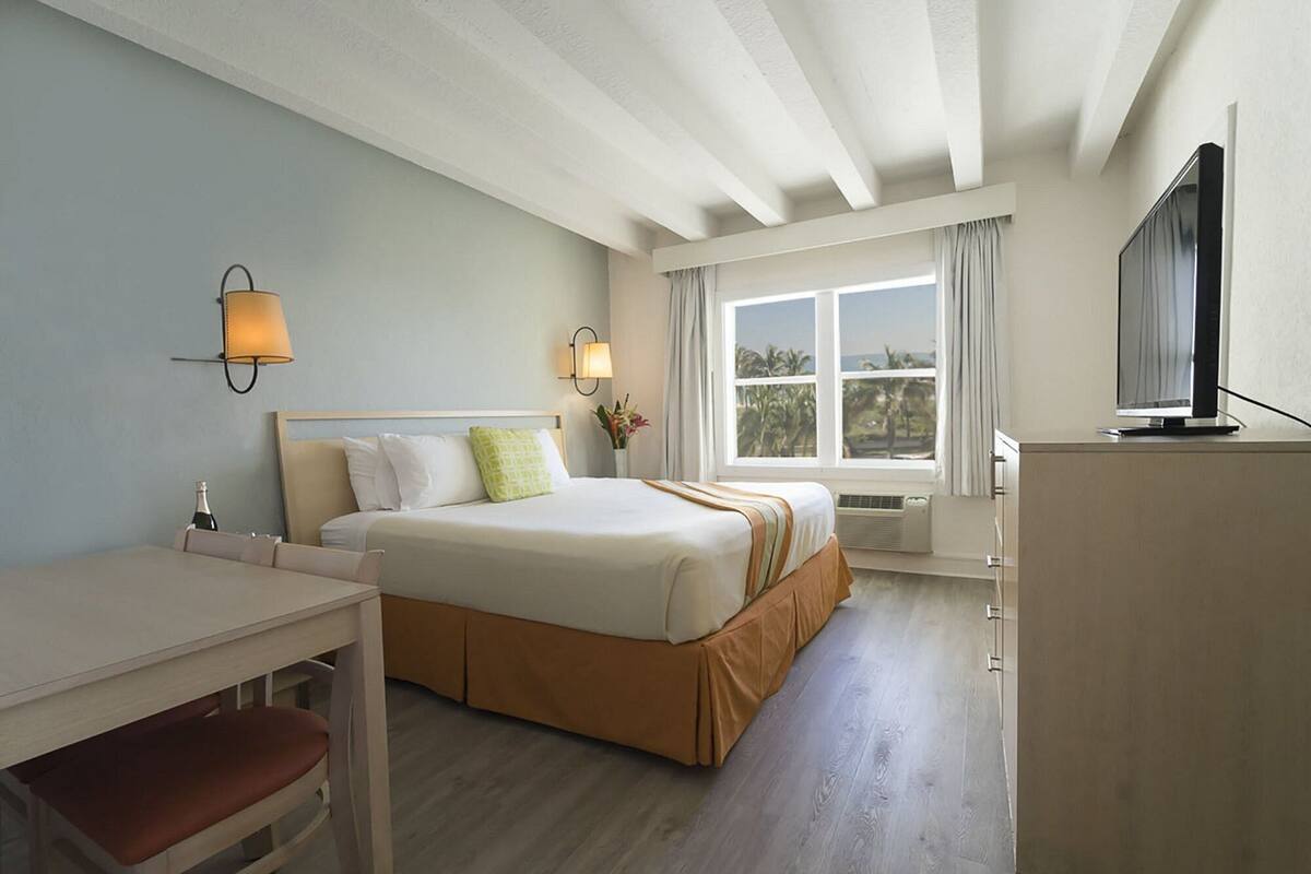 A hotel room with a bed, bedside table, lamp, TV, and a window with a view.