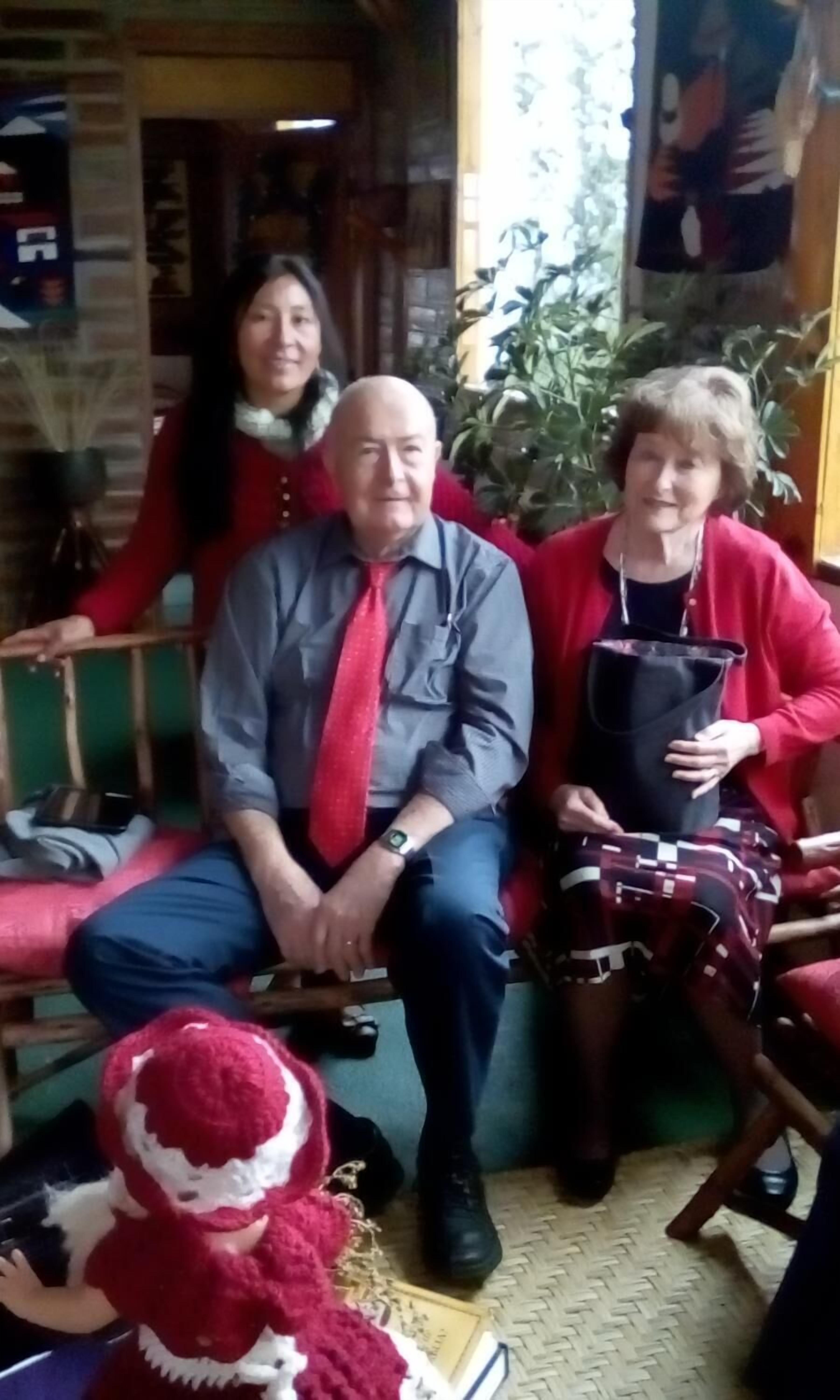 Un grupo de personas sentadas en un banco en una habitación con pared de ladrillo y una ventana.