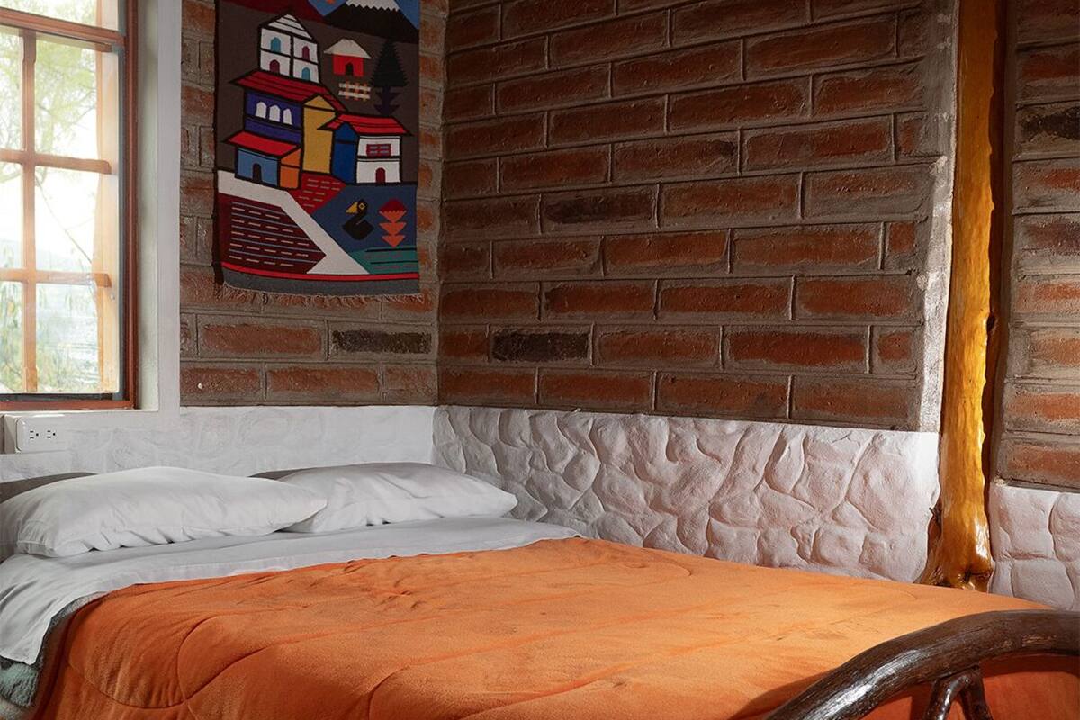 A bed with an orange blanket, a wooden headboard, and a brick wall with a colorful mural.