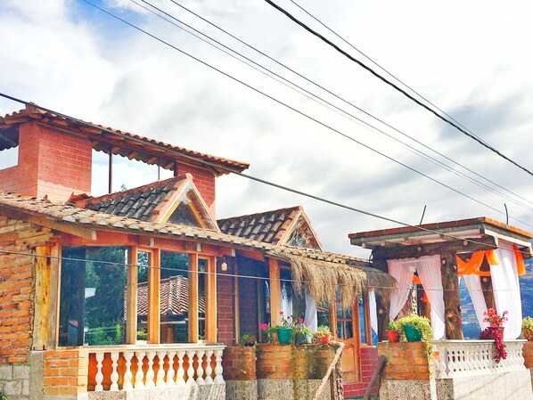A traditional house with a tiled roof, brick walls, and large windows. - Alojamiento Vertientes del Imbabura (San Pablo del Lago)