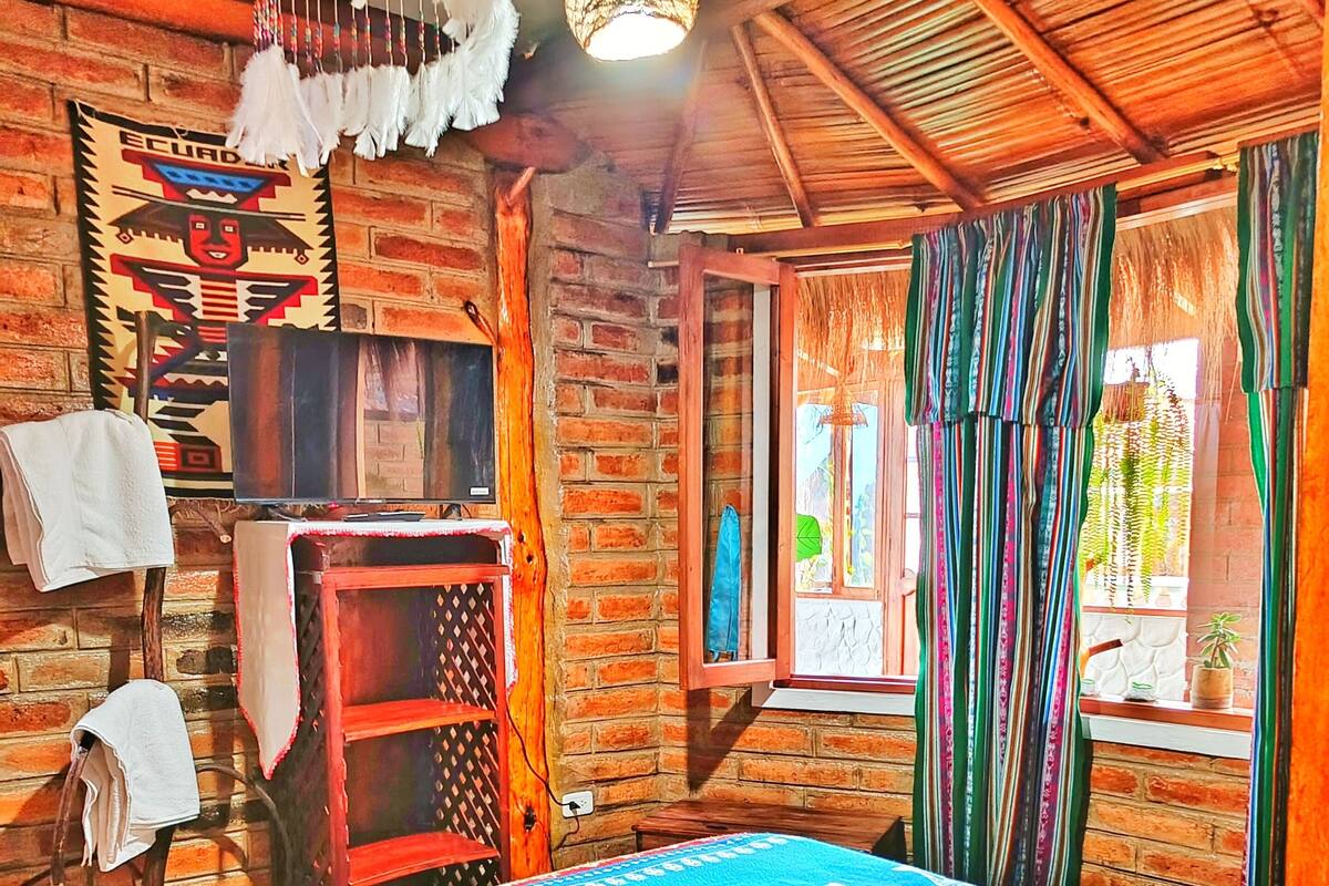 A room with a bed, a wooden shelf, a hanging light fixture, and a window with curtains.