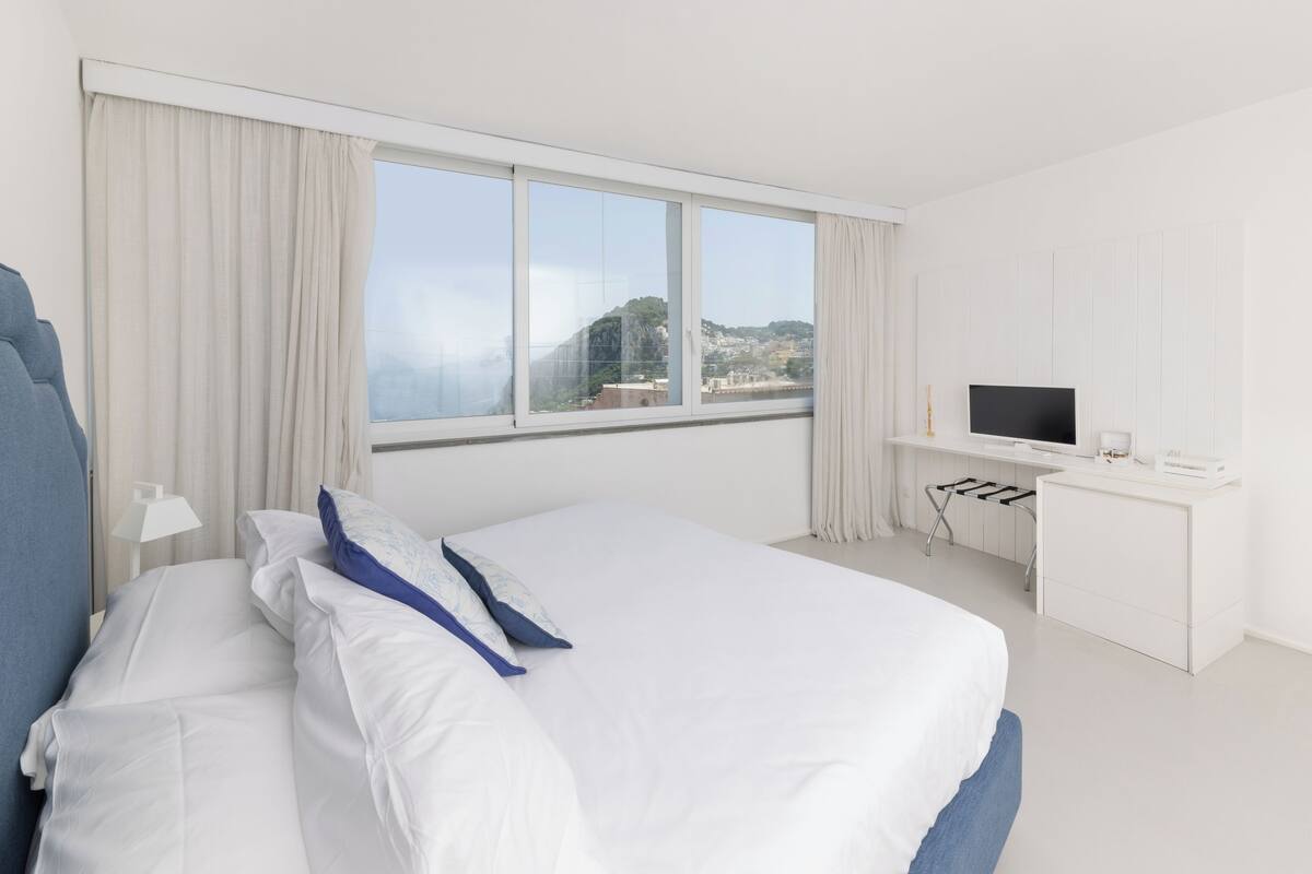 A hotel room with a large bed, a desk, a TV, and a view of a mountain.