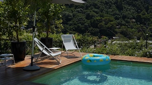 A wooden deck with a pool, lounge chairs, and a view of a hill. - Suite Time Capri Villa La Pergola (Capri)