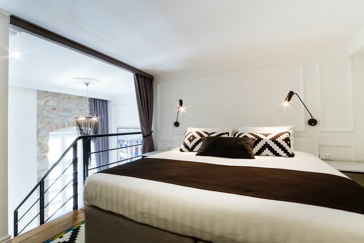 Ein Hotelzimmer mit einem großen Bett, einer Wand aus Stein, einem Balkon mit Geländer und zwei Wandleuchten.