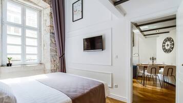 Un dormitorio con cama, televisor montado en la pared, ventana con cortinas y vistas a un comedor.