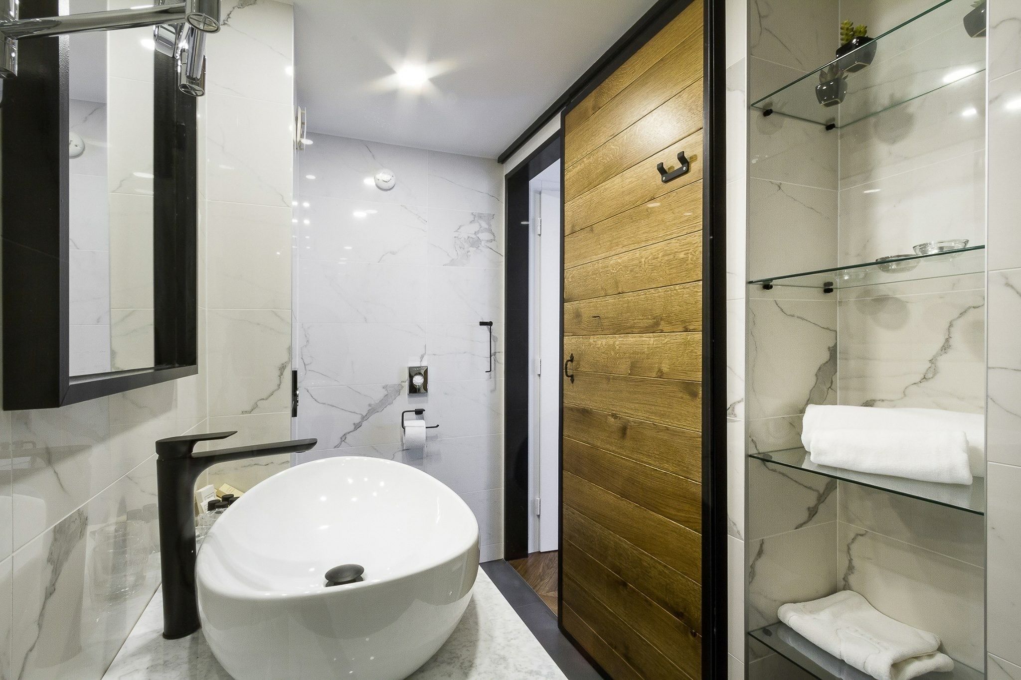 Une salle de bain moderne avec un grand lavabo blanc, une porte en bois et une cabine de douche en verre.