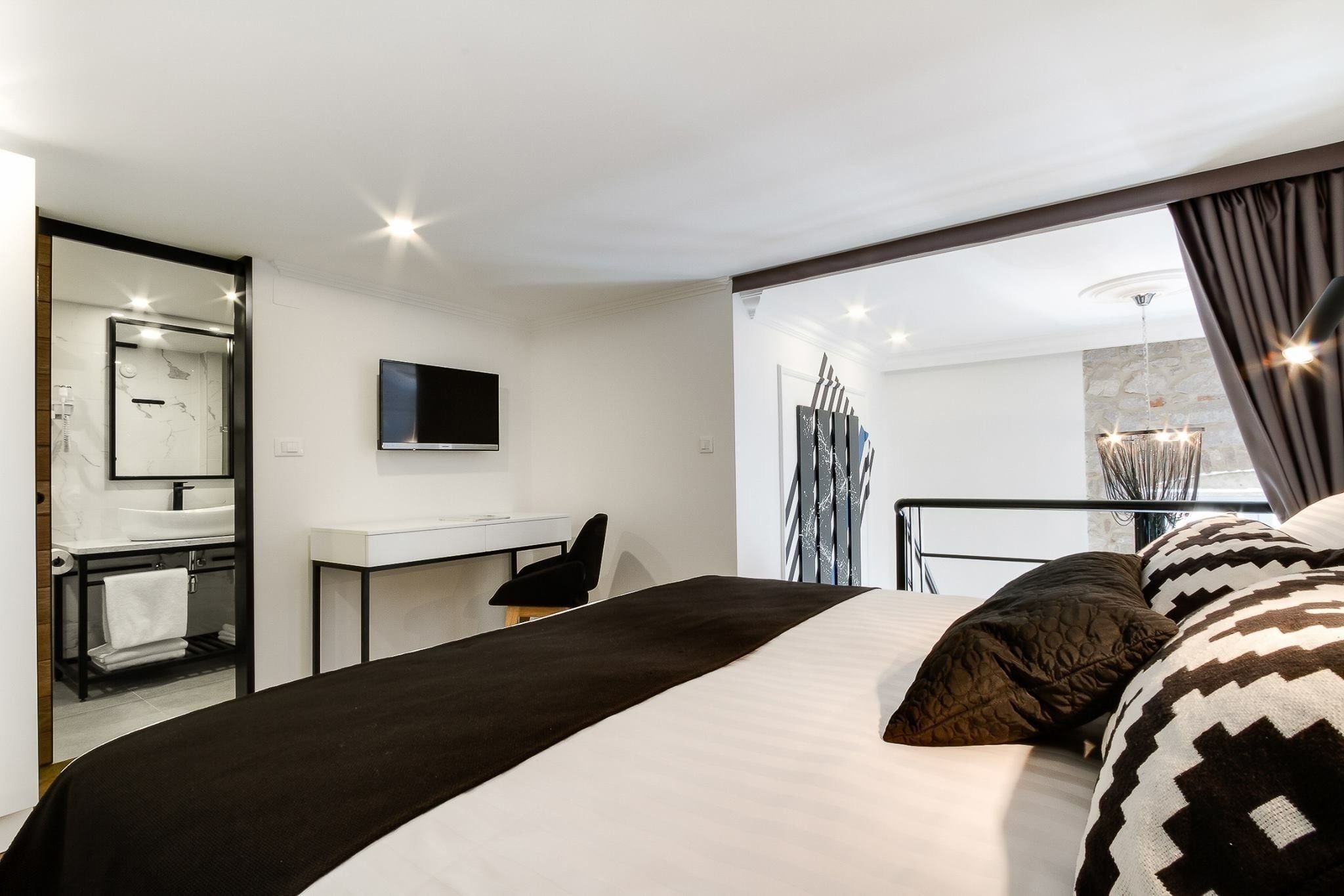 Habitación de hotel moderna con una cama grande, un escritorio, un televisor y un baño con espejo y lavamanos.