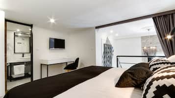 Habitación de hotel moderna con una cama grande, un escritorio, un televisor y un baño con espejo y lavamanos.