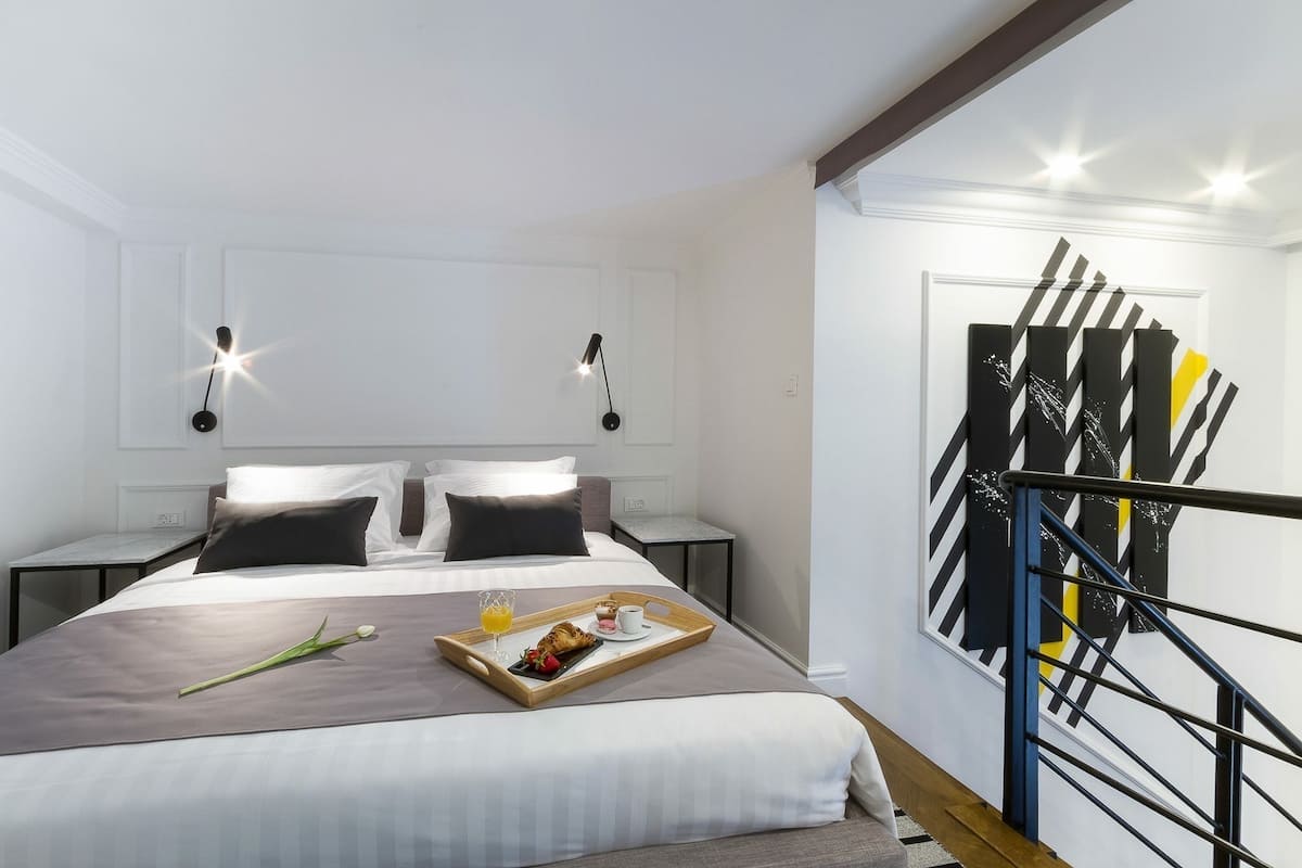 Ein modernes Hotelzimmer mit einem ordentlich bezogenen Bett, einem Tablett mit Frühstücksangeboten und einer Treppe mit einem markanten schwarz-gelben Design.