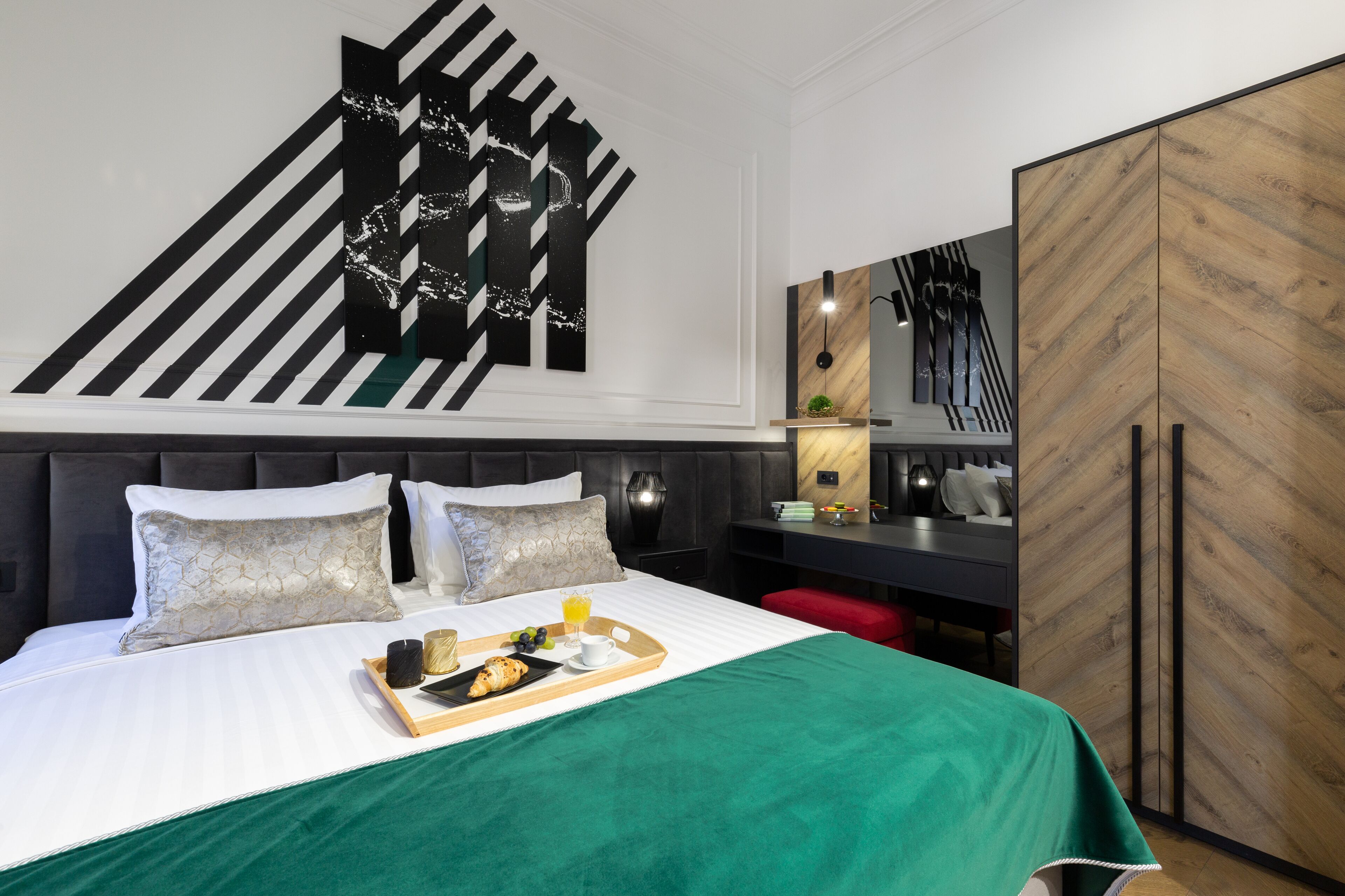 A modern hotel room with a large bed, a desk, and a wardrobe.