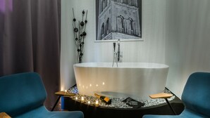 A modern bathroom with a freestanding bathtub, two blue chairs, and a decorative wall piece. - DeZign Apartments (Zadar)