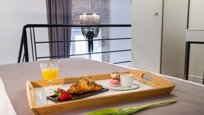 A breakfast tray with croissant, strawberries, a glass of orange juice, and a cup of coffee on a table in a room with a modern design, including a chandelier and a stone wall. - DeZign Apartments (Zadar)