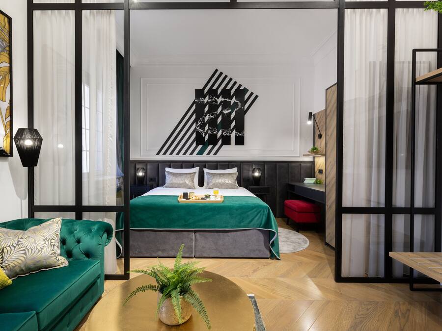 A modern bedroom with a green sofa, a bed with a green bedspread, a wall art piece, and a small table with a plant.
