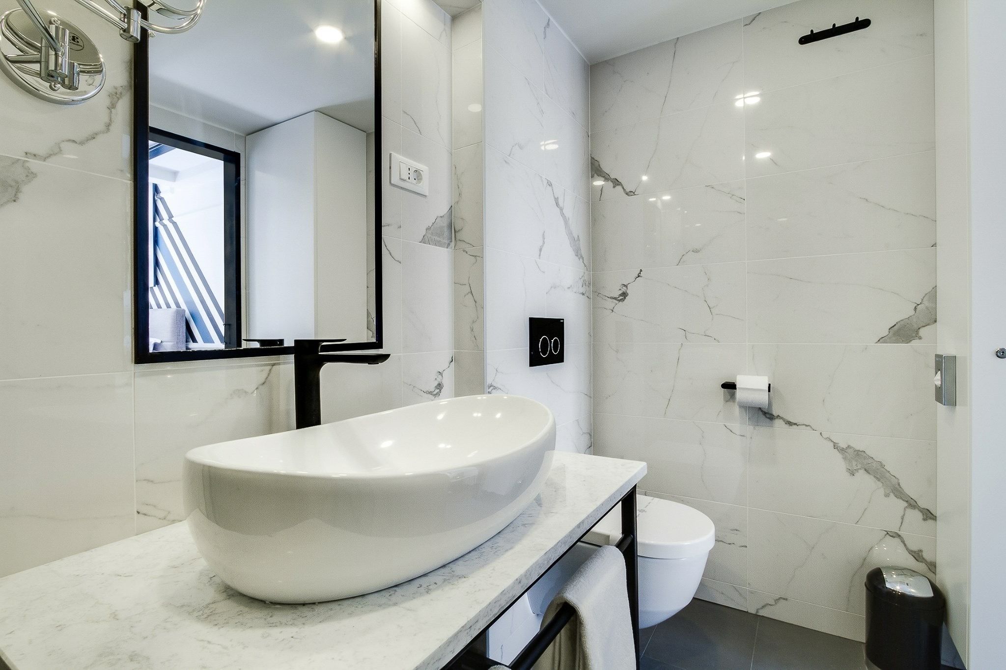 A modern bathroom with a large white marble sink, a mirror, and a toilet.