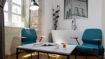 Un baño moderno con una bañera, dos sillas azules, una mesa con una revista y un adorno de pared.