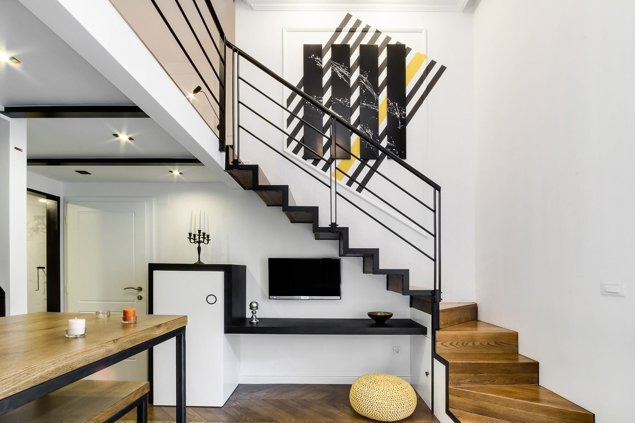 A modern staircase with a black railing, a flat-screen TV mounted above, and a decorative wall piece.