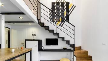 A modern staircase with a black railing, a flat-screen TV mounted above, and a decorative wall piece.