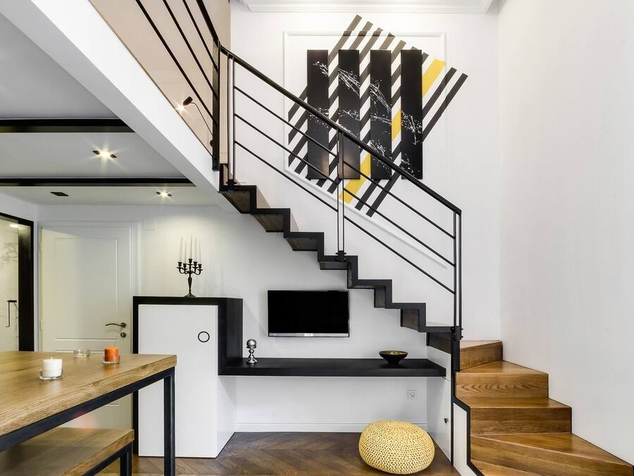 A modern staircase with a black railing, a flat-screen TV mounted above, and a decorative wall piece.