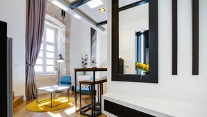 A modern living room with a wooden floor, a round coffee table, a blue chair, and a large window with curtains. - DeZign Apartments (Zadar)