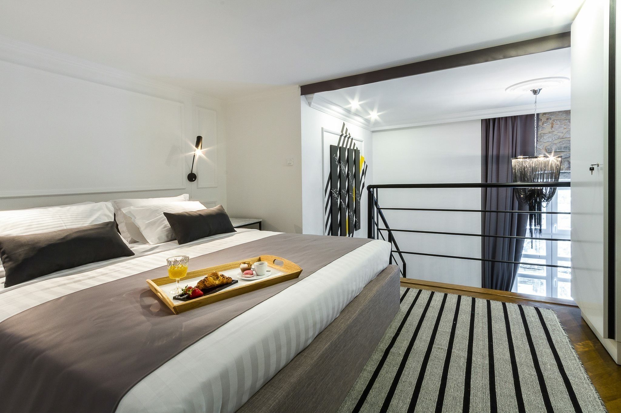 A modern hotel room with a large bed, a breakfast tray, a balcony with a view, and a stylish chandelier.