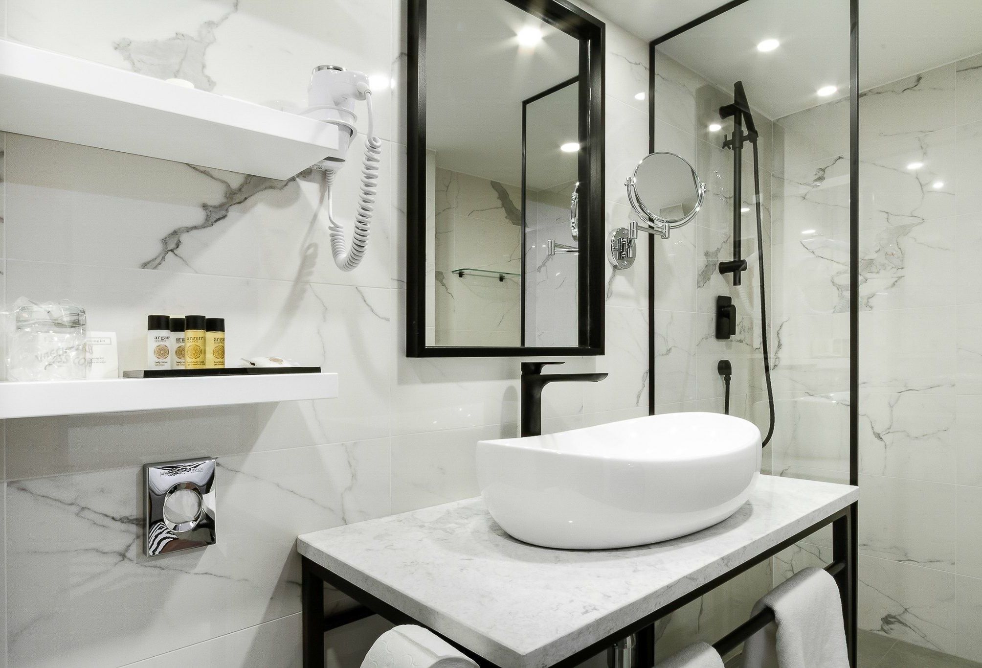 A modern bathroom with a white sink, a large mirror, and a glass-enclosed shower.