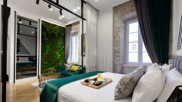 A modern hotel room with a bed, breakfast tray, green sofa, and a green wall. - DeZign Apartments (Zadar)