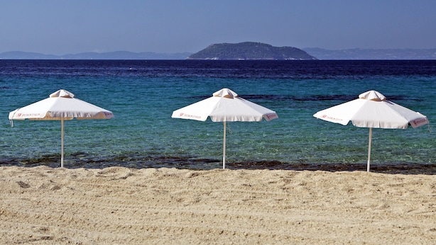 Drie witte strandparasols op een zandstrand met helderblauw water en een eiland in de verte.