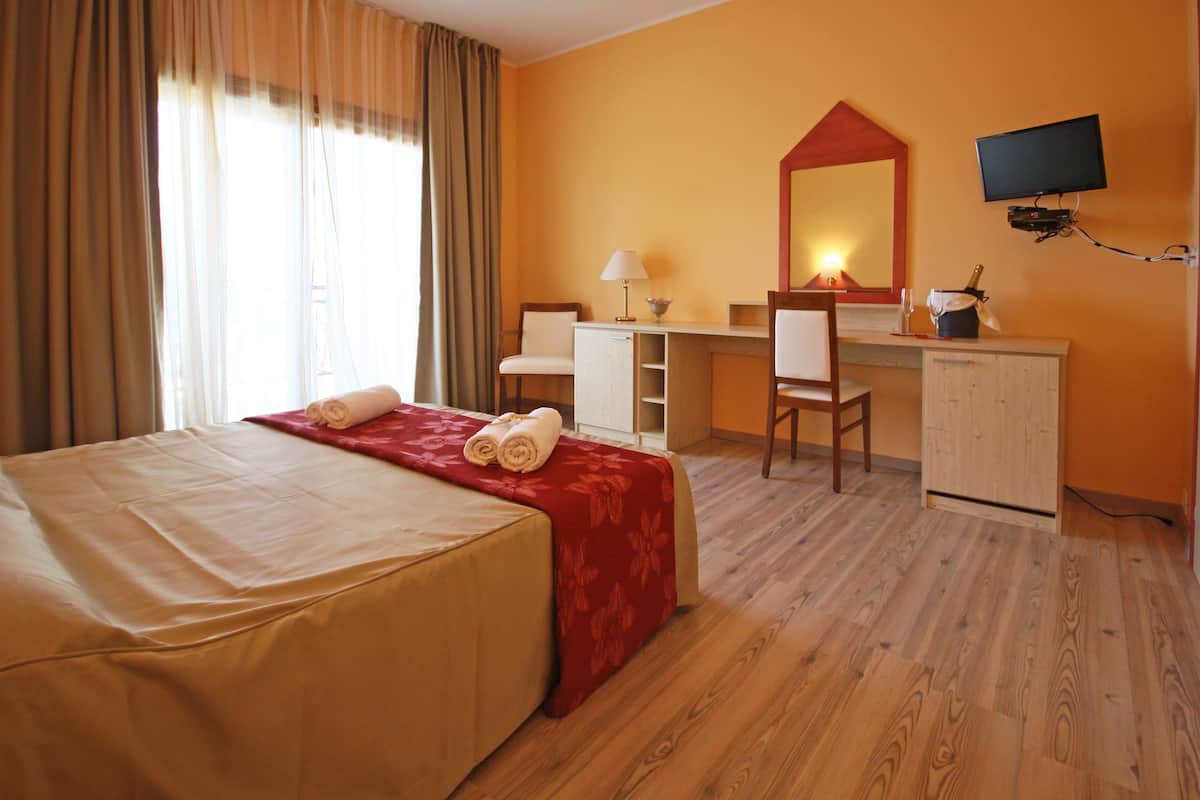 A hotel room with a bed, a desk, a chair, a television, and a minibar.