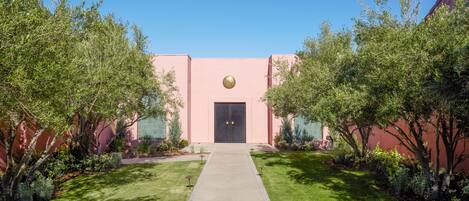 A building with a pink facade, a black door, and a paved walkway leading to it.