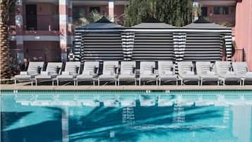 A poolside area with lounge chairs and umbrellas, a clear pool, and a building with a red-tiled roof and balconies.