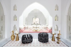 A room with a white arched window, a pink sofa, two ottomans, and a small table with candles. - Sands Hotel and Spa (Indian Wells)