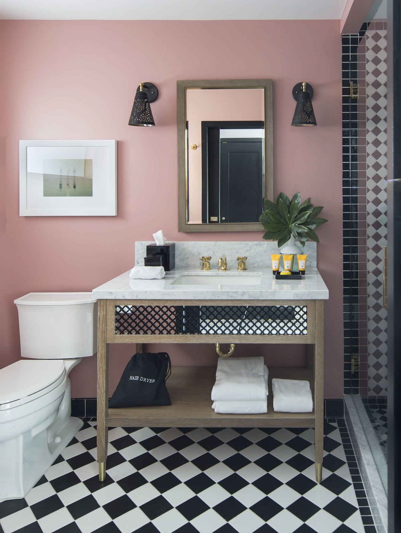 A bathroom with a white toilet, a sink with gold faucets, a mirror, and a framed picture on the wall.